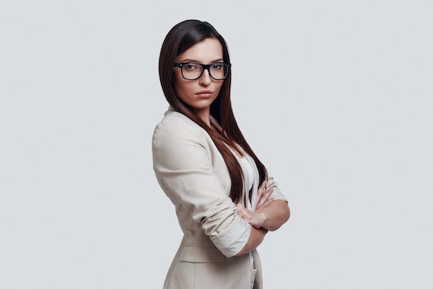 Serious expertise. Attractive young woman looking at camera while standing against grey background