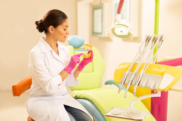 Serious female dentist holding an artificial teeth model