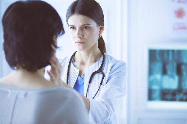 A serious female doctor examining a patient's lymph nodes