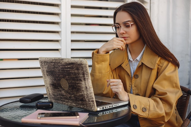 Serious female freelancer in glasses reading from laptop screen and working on remote project