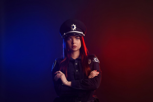 Serious female police officer is posing for the camera against a black background with red and blue ...