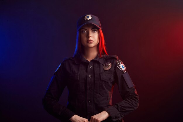 Serious female police officer is posing for the camera against a black background with red and blue ...