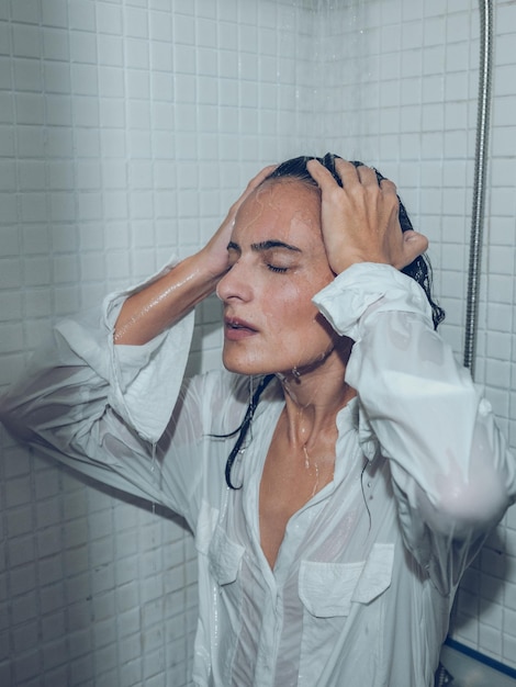 Serious female in white shirt touching wet hair while taking shower in cabin and relaxing