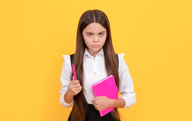 Serious frown child hold school book and pen yellow background learning