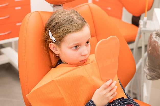 Serious girl looking at mirror in the dentists chair