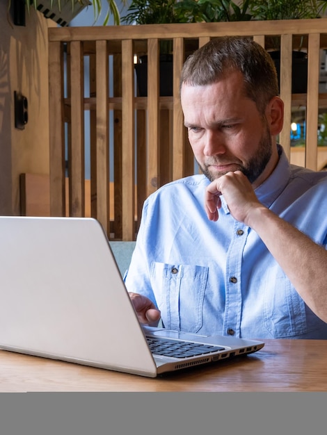 Serious handsome arabian man with beard is using laptop reading email typing on keyboard in cafe Handsome male freelancer working on laptop at workplace Businessman typing information