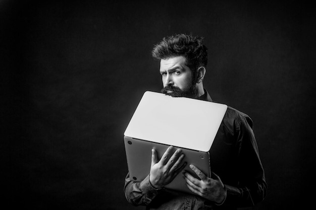 Serious handsome bearded man worker laptop Bearded male businessman holding a computer in his hands isolated on black background Black and white