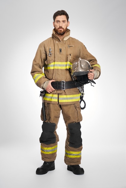 Serious handsome caucasian firefighter in full gear looking at camera indoors front view of strong