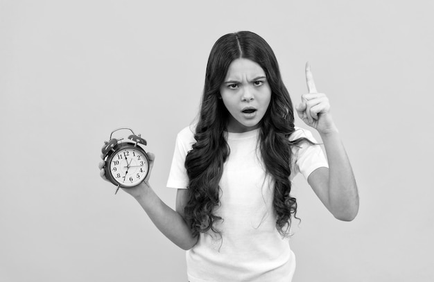 Serious kid hold retro alarm clock showing time with raised finger discipline