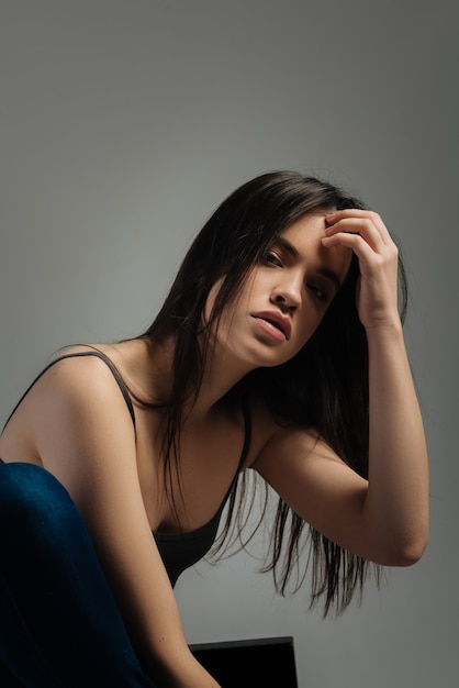 Serious lady. Beautiful unsmiling long-haired young woman sitting and staring and touching her hair