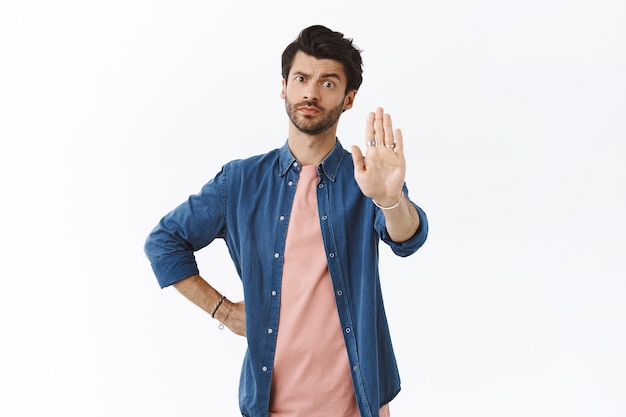 Serious-looking concerned and assertive handsome man, raise one arm in prohibition, warning motion, smirk displeased and look skeptical, judgemental at camera, forbid something