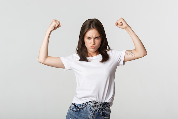 Serious-looking confident brunette girl flex biceps, showing strengths.