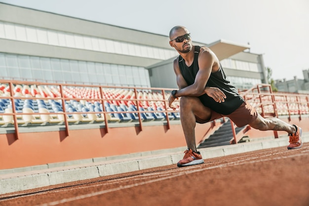 Serious male athlete in sunglasses standing on the running track at the stadium