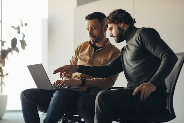 Serious male colleagues working together using laptop computer at contemporary company office blank space