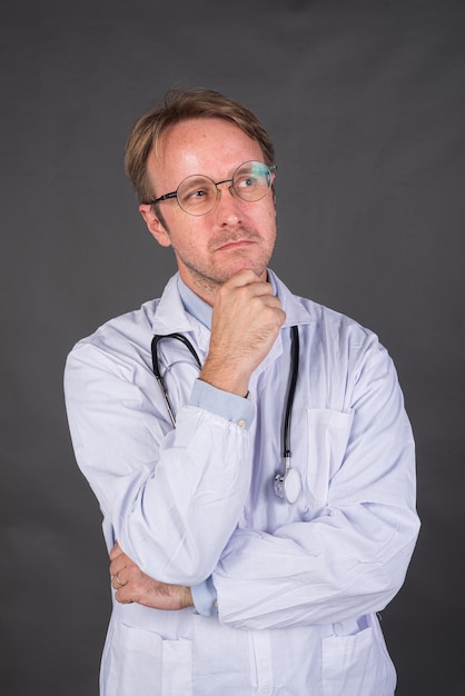 Serious male doctor with stethoscope over neck in medical coat thinking and looking up