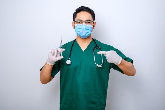 Serious male nurse or doctor in green scrubs medical mask pointing at syringe with coronavirus vaccine