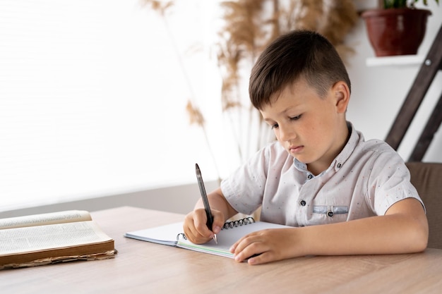 Serious male student doing handwritten homework in a notebook while sitting in class at the table Preparing an elementary school boy for tests Getting education and knowledge Homeschooled