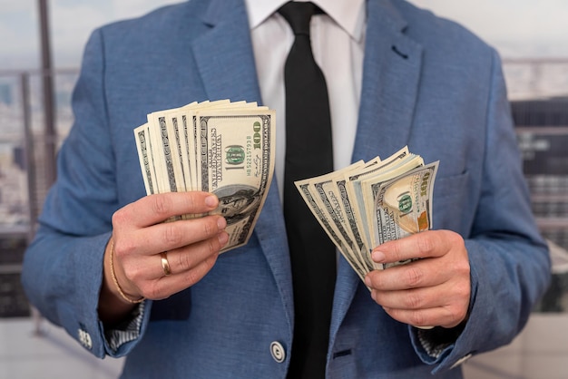 Serious man in elegant suit holds a bunch of money to invest in a new business project Business and profit concept