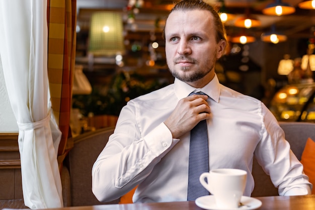 Serious man looking away  sitting in the restaurant  indoor wearing in white shirt and straightening tie