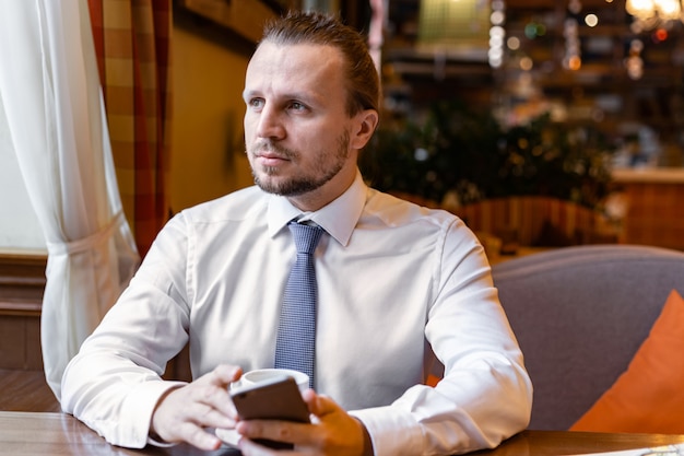 Serious man sitting in the cafe bar holding in his hand a  mobile phone during coffe break. 