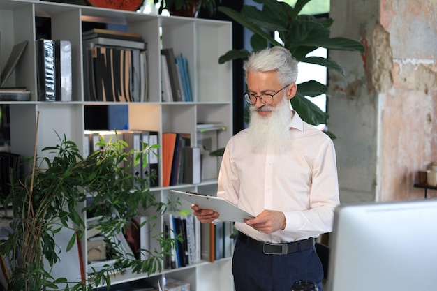 Serious mature business man in white shirt reading contract while standing in the office