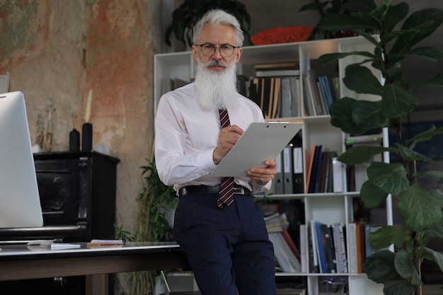 Serious mature business man in white shirt reading contract while standing in the office.