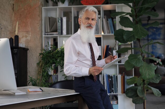 Serious mature business man in white shirt reading contract while standing in the office.