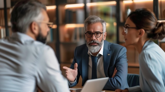 Serious mature businessman in eyeglasses looking at camera during meeting with colleagues in office