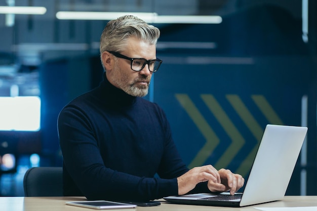 Serious mature grayhaired businessman working inside modern office man thoughtfully typing on laptop