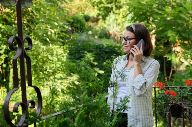 Serious mature woman talking on the phone, female at home on an open landscaped balcony, copy space