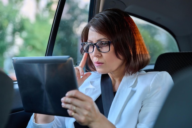 Serious middleaged business woman in car in passenger backseat