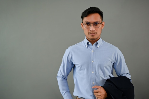 Serious millennial Asian businessman holding his suit isolated grey background