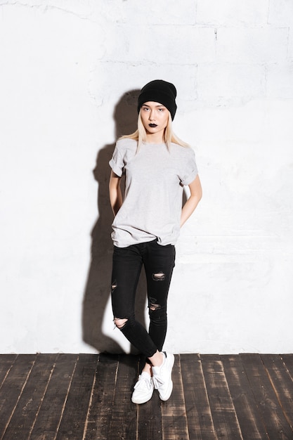 Serious modern young woman with black lips in hat standing