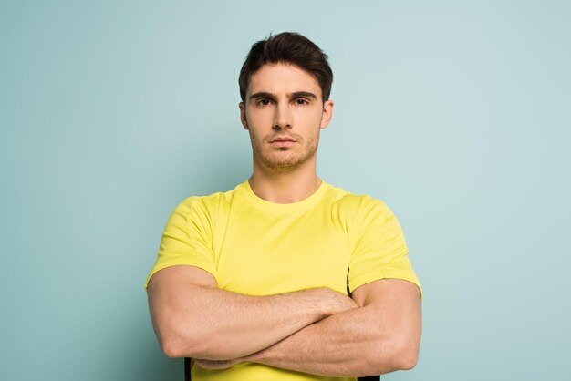 Serious muscular sportsman with crossed arms on blue