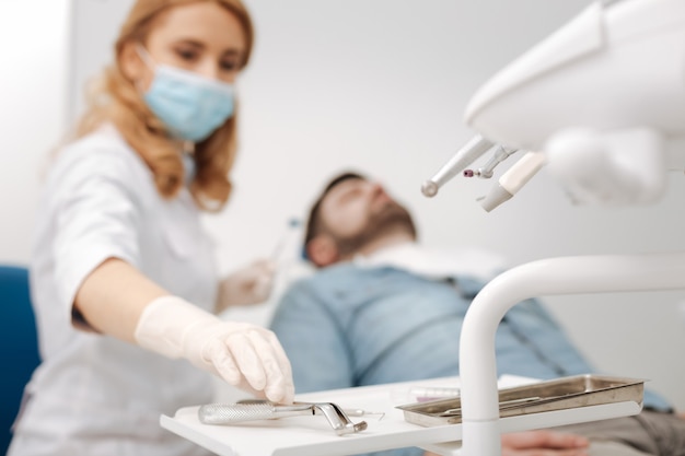 Serious prepared distinguished dentist reaching for her sterile tool while needing it for extracting patients tooth