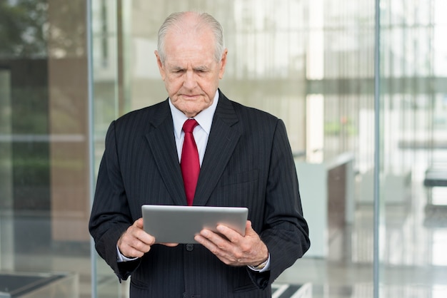 serious senior business man using tablet computer with glass wall