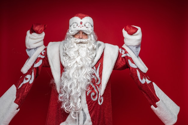 Serious senior male in xmas Santa Claus costume posing on red background celebrating new year