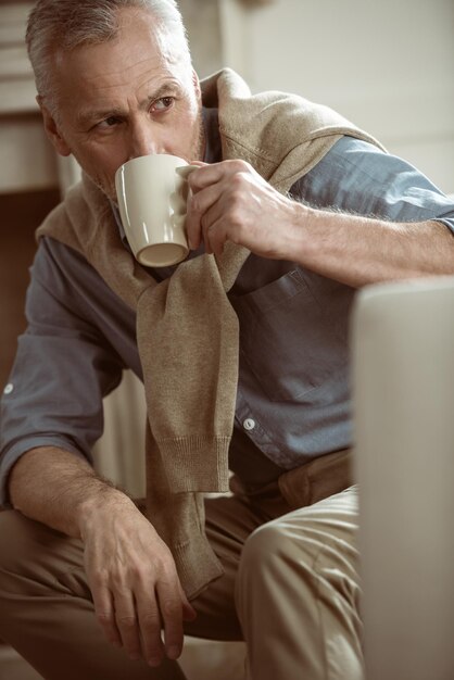 Serious senior man sitting with cup of tea and looking away