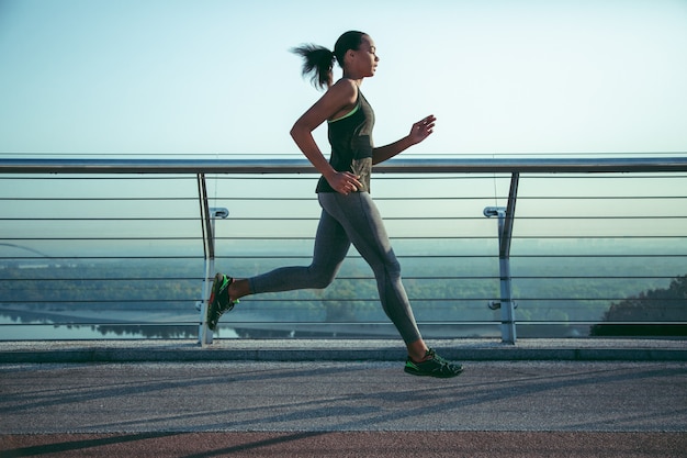 Serious sportswoman running on the bridge in sports clothes