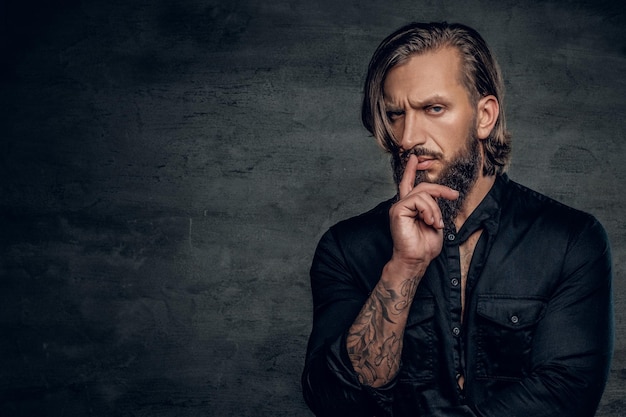 Serious stylish bearded male with tattooed arm wearing black shirt.