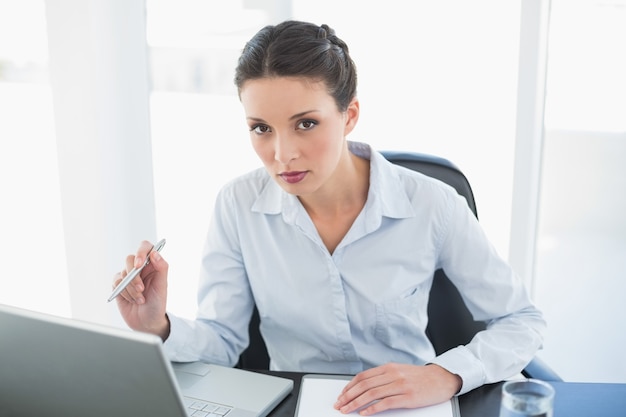 Serious stylish brunette businesswoman pointing her laptop with her pen