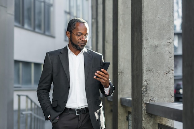 Serious and successful african american boss businessman outside office building using smartphone