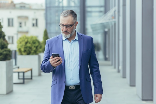 Serious and successful senior grayhaired businessman walking outside office building man holding