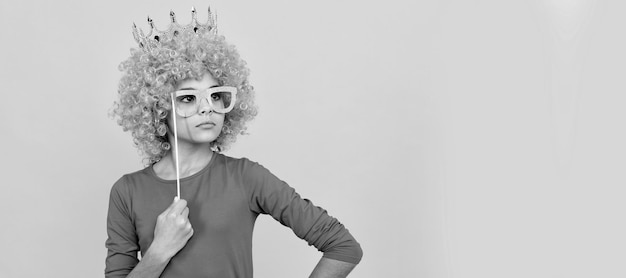 Serious teen girl in fancy clown wig wear queen crown and funny party glasses arrogant Funny teenager child in wig party poster Banner header copy space