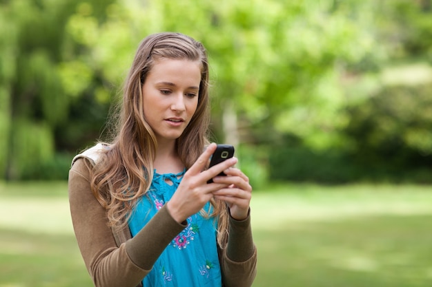 Serious teenage girl sending a text while standing in a park