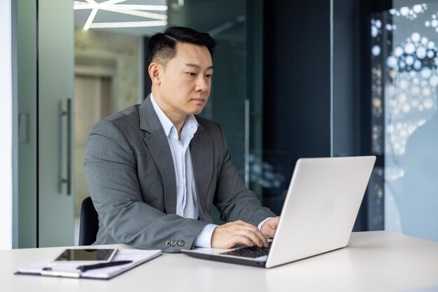 Serious and thoughtful businessman working inside office sitting at table using laptop at work