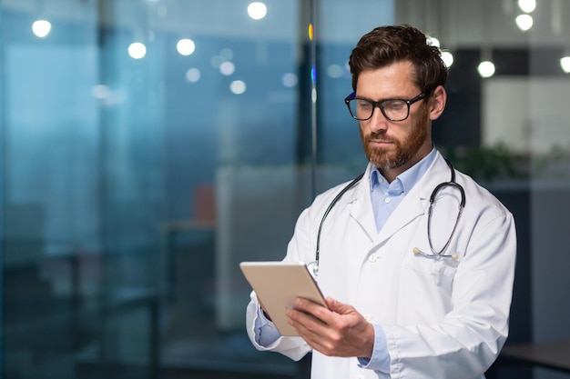 A serious and thoughtful doctor reads medical information from a tablet computer a man in a medical