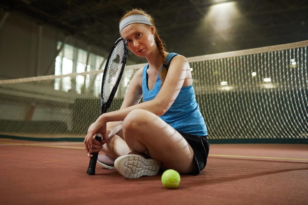 Serious woman sitting on tennis court