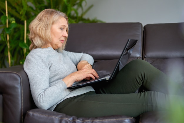 Serious woman using laptop checking email news online sitting on sofa