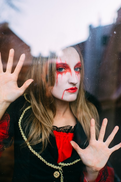 Serious woman in witch costume poses behind glass